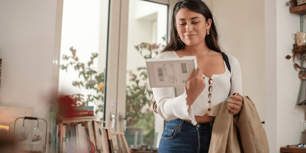 une femme reçoit un paquet et sourit, saitsfaite de l’expérience post-achat 